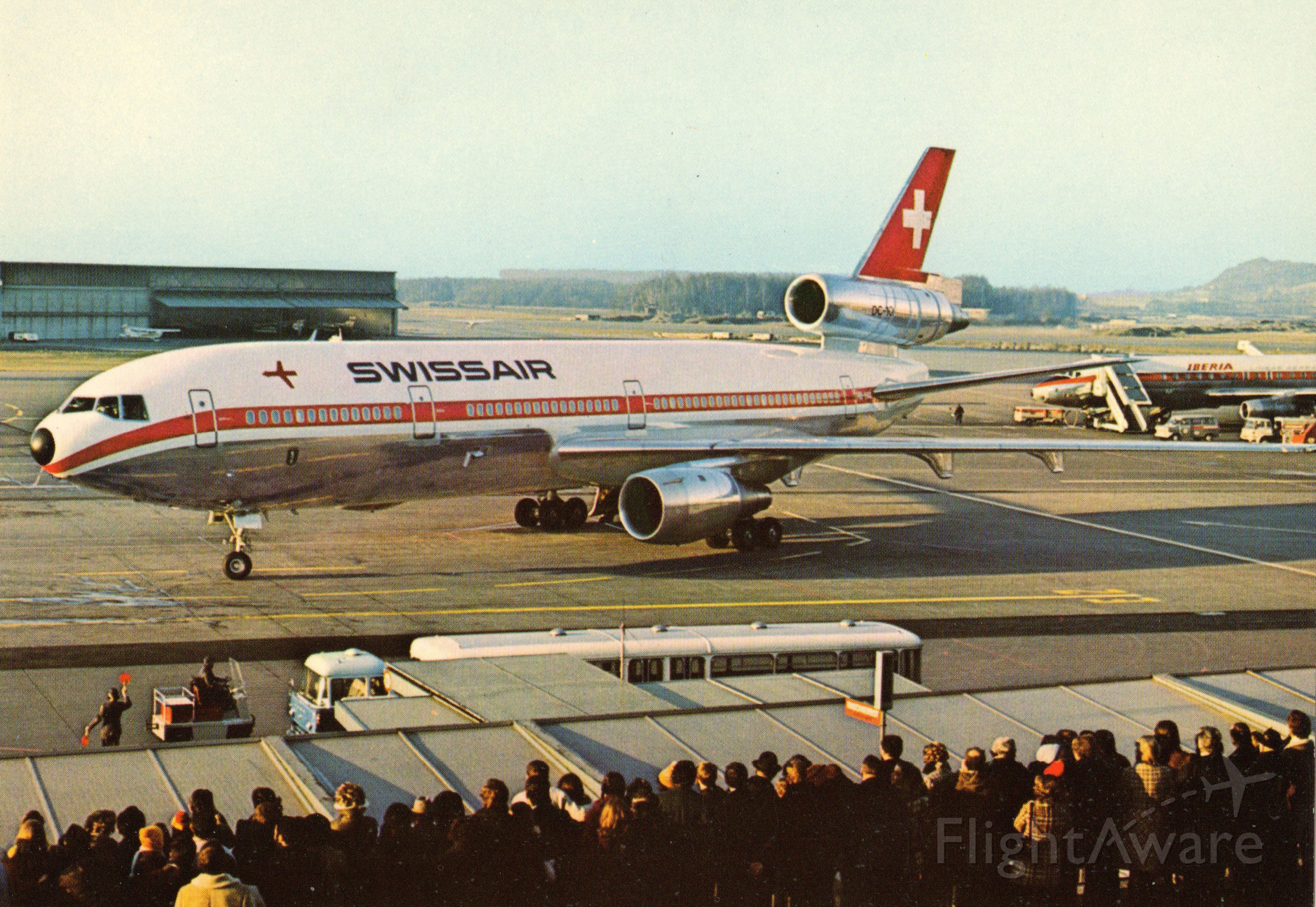 McDonnell Douglas DC-10 (HB-IHA) - This is a postcard I purchased back in the early 1970's. I did not photograph this image! It depicts a McDonnell Douglas DC-10-30 arriving with folks viewing the aircraft above the arrival gate. Also in the scene is a partial front part of the national airlines of Spain, Iberia. A commenter has noted that Iberia is a DC-8-52. br /Cielo despejado para nuestros miembros espanoles.